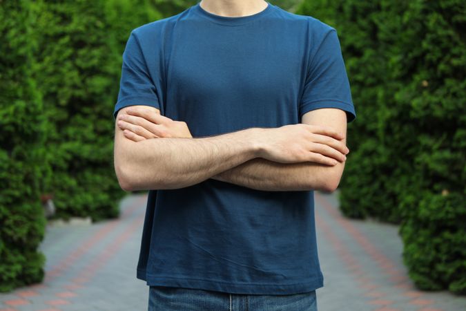 Young man in a blank t-shirt stands with folded hands