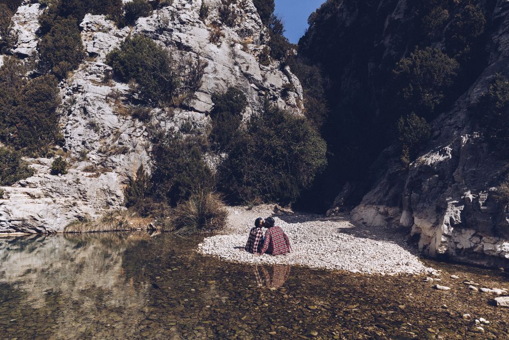 Positive woman and man resting and kissing on stone shore near river