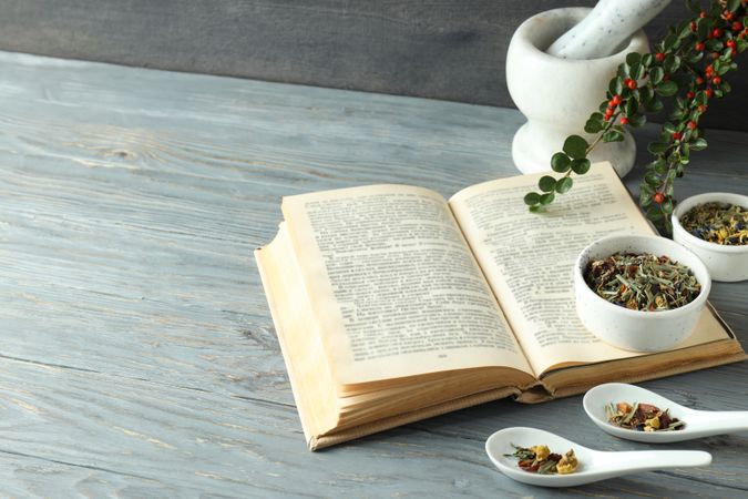 Book and herbs in scoops and bowls on wooden background, space for text