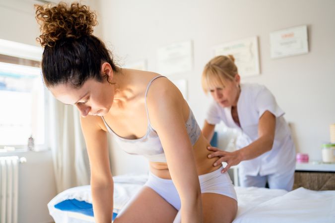 Osteopath checking lower back of female patient