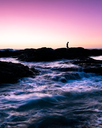 Silhouette of person standing on rock formation on sea water during sunset