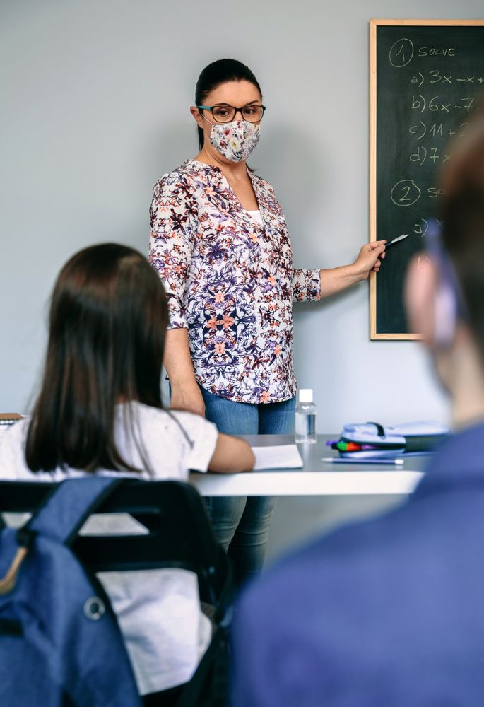 Teacher with mask explaining exercises in math class