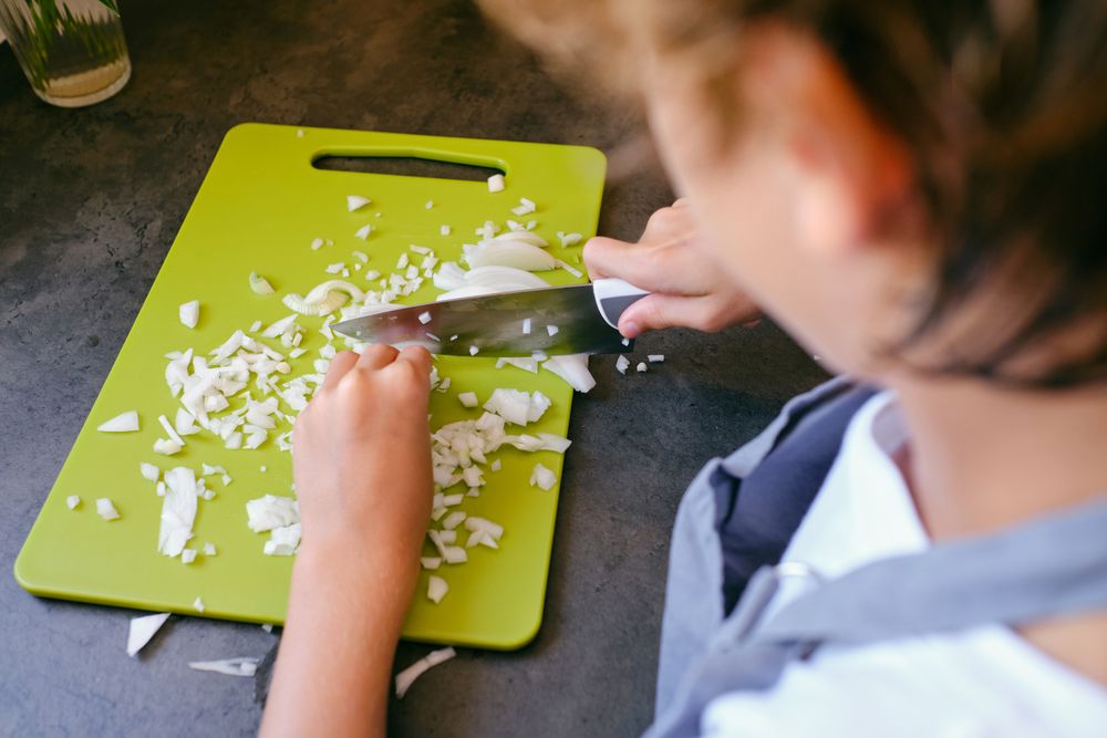 Crop boy chopping fresh onion while cooking in kitchen