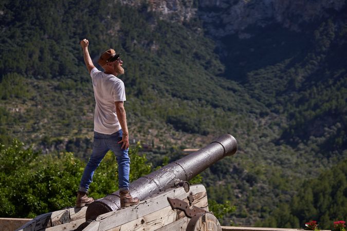 Male tourist standing on old cannon and enjoying mountain view