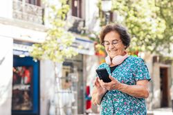 Older woman using smartphone and headphones walking down the street