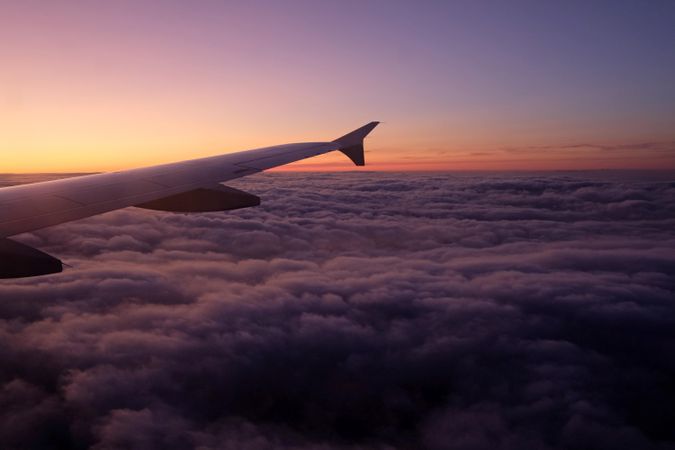 Window seat view of airplane wing over clouds during sunset