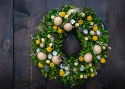 Easter card concept with fresh wreath with decorative eggs and feathers hanging on door