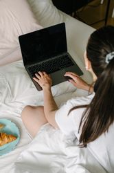 Crop woman using laptop on bed having breakfast