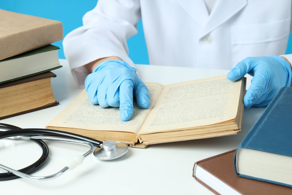 Books and stethoscope on light table, doctor on blue background