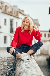 Laughing young blond woman sitting on rocky stoop in Spanish town