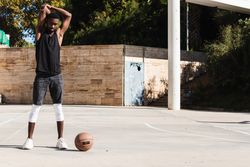 Black sportsman stretching on basketball court