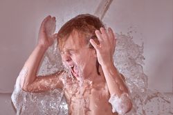 Boy under pouring water in bathtub
