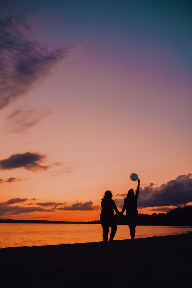 Unrecognizable females walking along beach during sunset