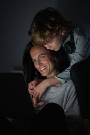 Smiling mother and son watching movie on laptop together while h