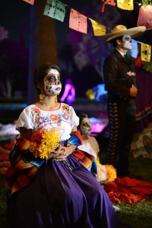 Woman sitting at altar for Day of the Dead wearing traditional makeup and dress