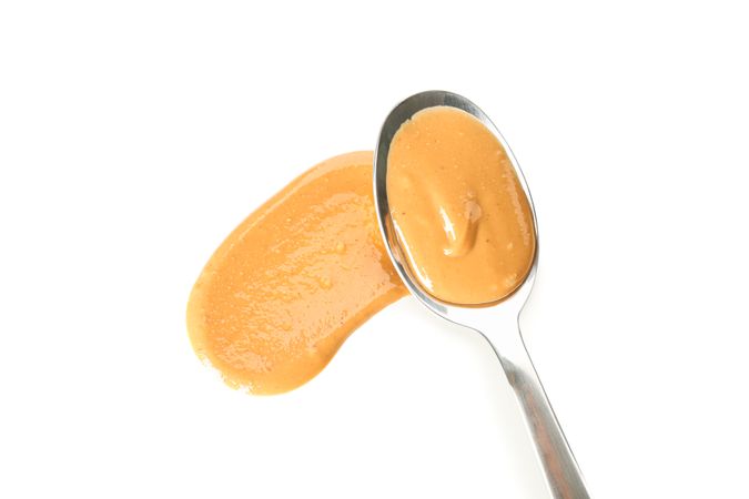 Spoon with creamy peanut butter isolated on light background, top view. A traditional product of American cuisine