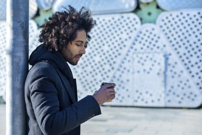 Side view of Black man in jacket with warm beverage standing outside