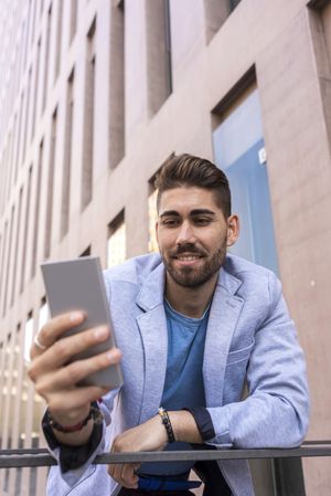 Portrait of happy man smiling while using his mobile phone standing outside, vertical