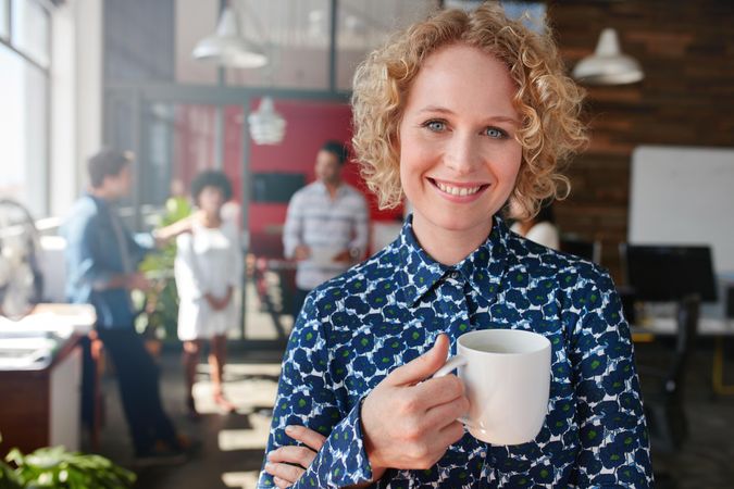 Happy professional woman holding cup of coffee in office