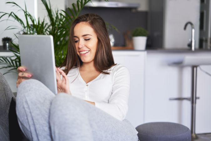 Smiling woman browsing on tablet and sitting on settee