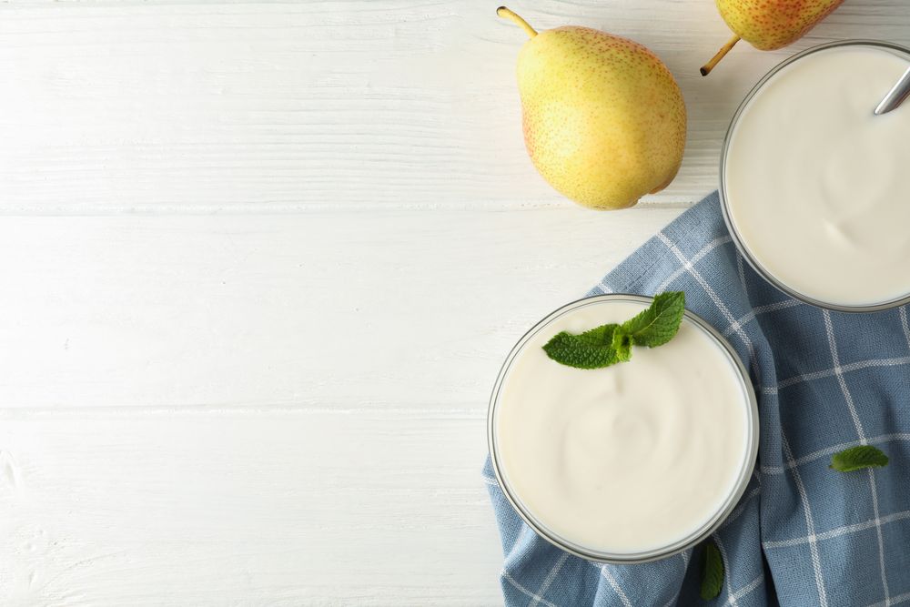 Cream yogurt, pears, towel and mint on wooden background, top view