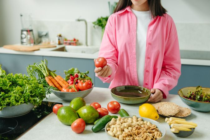 Cropped image of young woman in pink shirt standing beside vegetables on kitchen counter