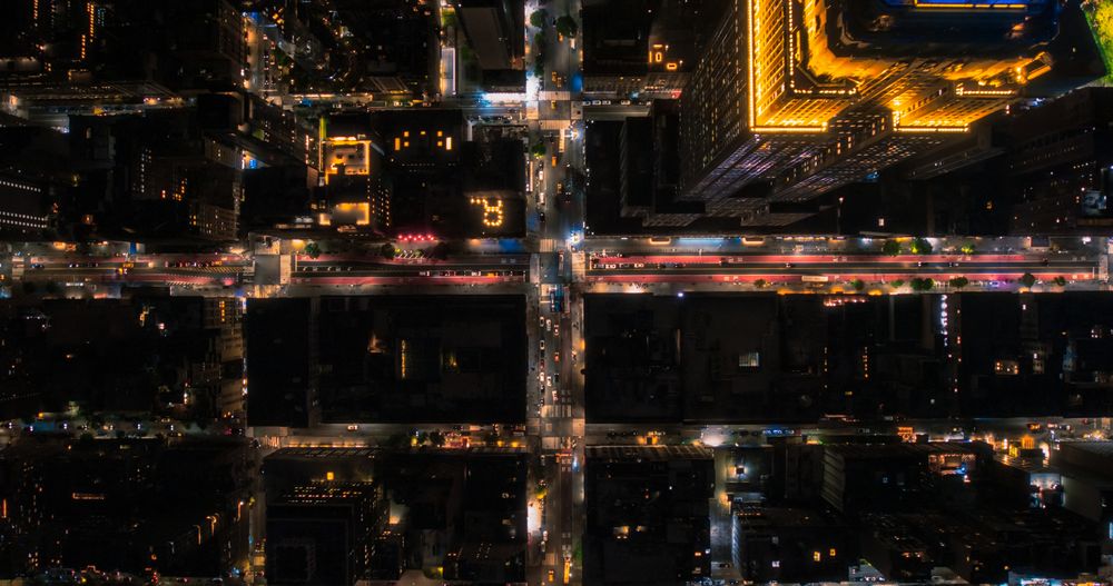 Top Down Aerial View of New York City Streets at Night with Visible Grid System, Business and Residential Building Roofs. Busy Center with Traffic, Cars, Yellow Taxis, Commercial Vehicles, Pedestrians