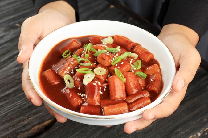 Person's hands holding bowl of Korean rice cakes in spicy sauce