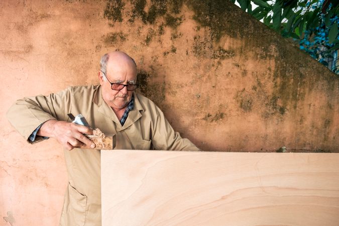 Older man shaping wood with plane tool