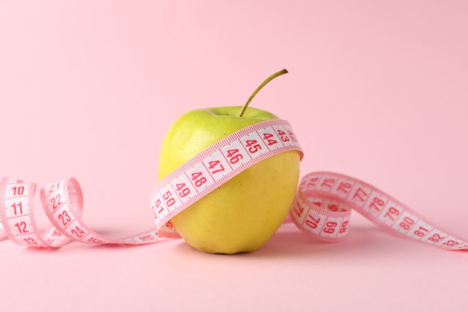 Measuring tape with apple on pink background, weight loss