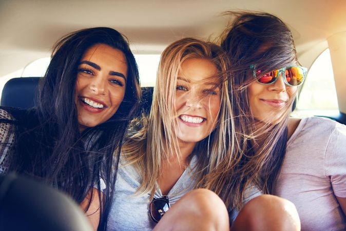 Group of female friends smiling at camera while riding in back of vehicle