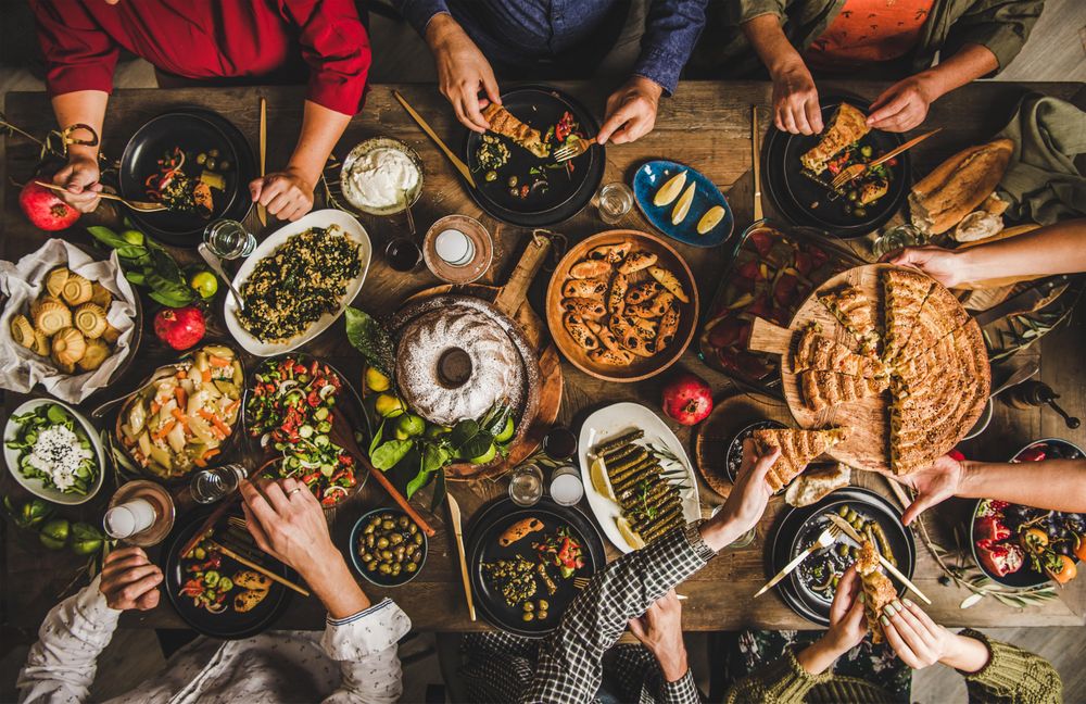 Group of people at wooden table with meze feast, serving flat bread