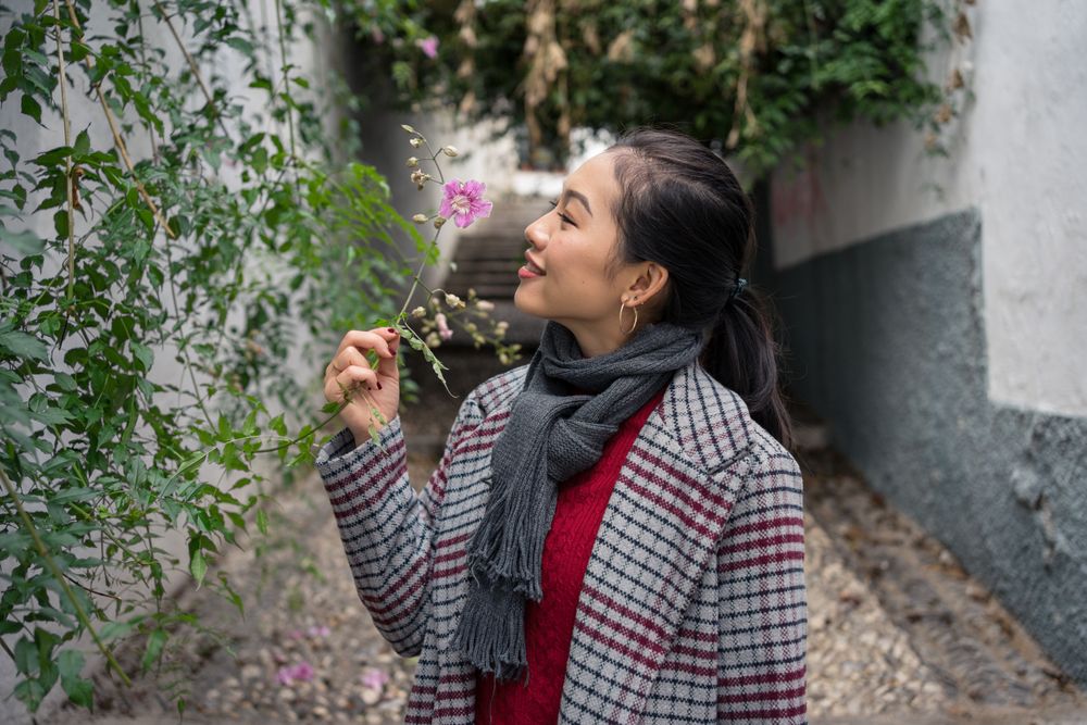 Young female in casual clothing touching green plants and smiling at rocked lane