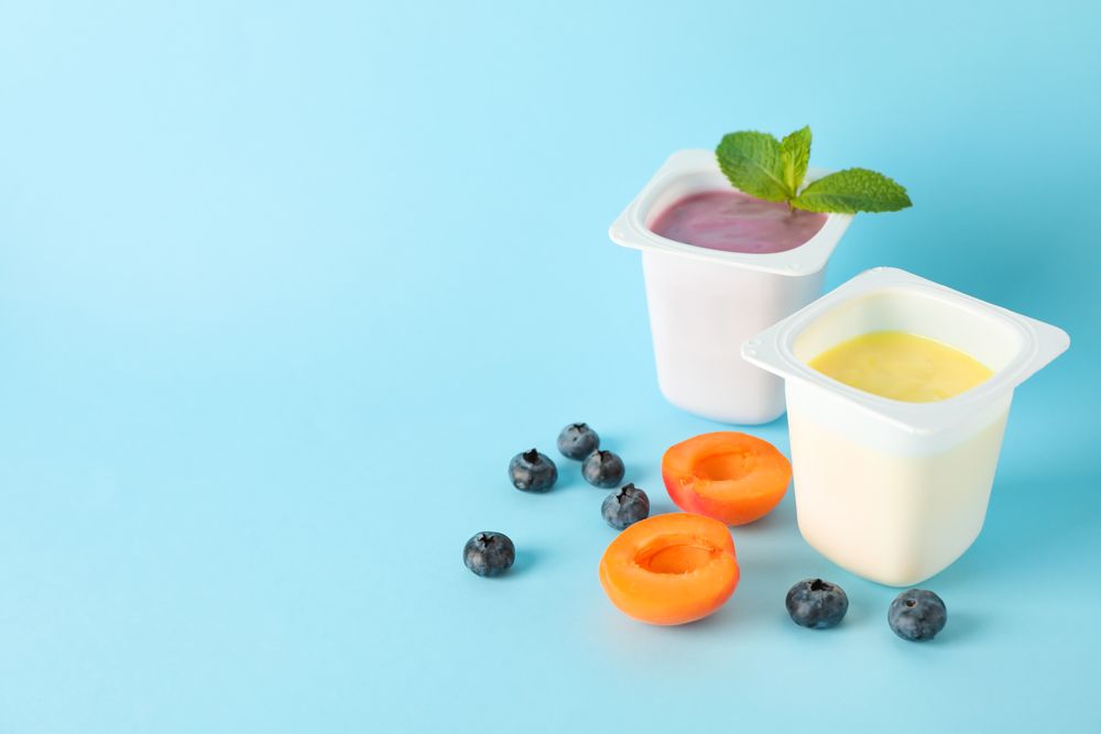 Plastic cups with yogurt and fruits on color background, space for text