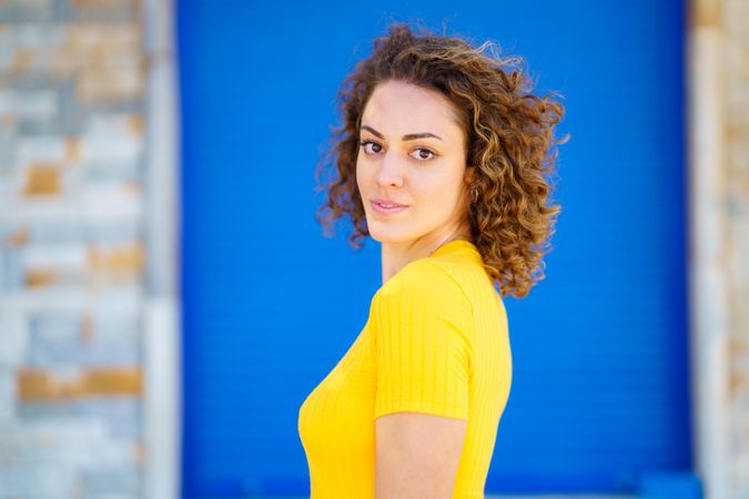 Woman looking around in front of blue background on outdoor wall