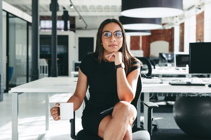 Creative businesswoman sitting alone in a modern office sitting with hand on her chin