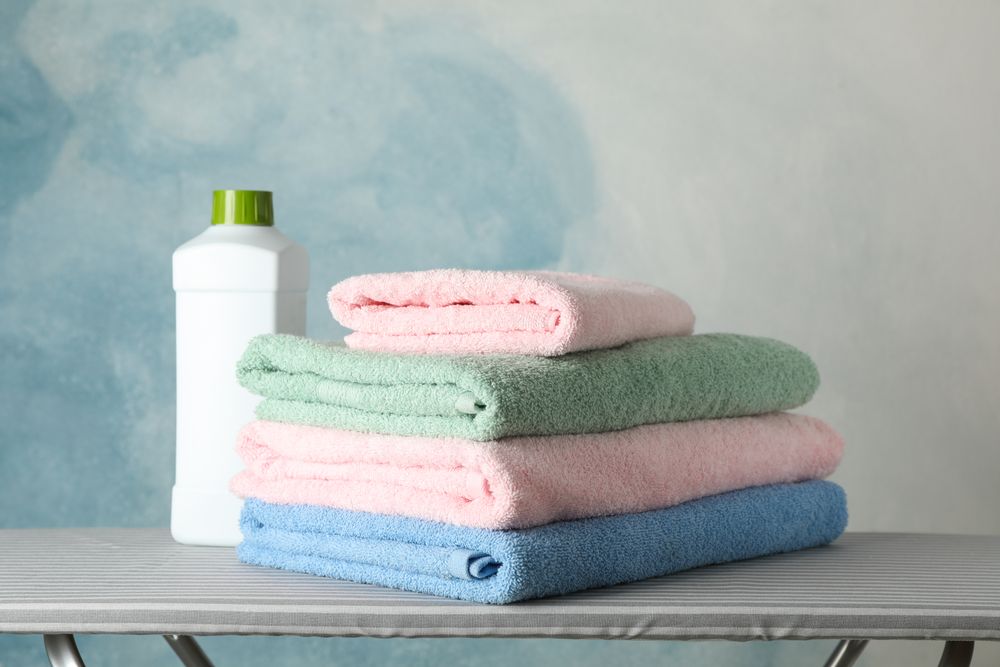 Stack of clean towels and laundry liquid on ironing board, copy space