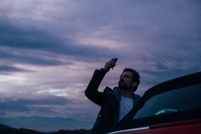Man leaning out of car taking picture at dusk