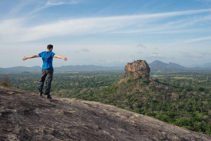 Tourist against solitary rock in middle of green forested plain under clear sky in summer