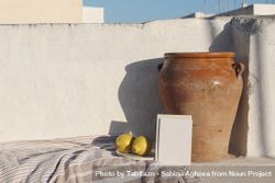 Blank greeting card, invitation mock up in sunlight leaning on vintage olive clay pot and fresh lemons fruit 0WOQGj