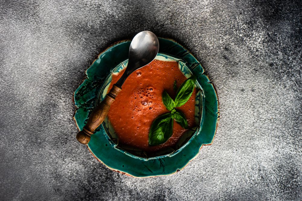 Top view of traditional Spanish tomato soup Gazpacho served with basil in green bowl with copy space