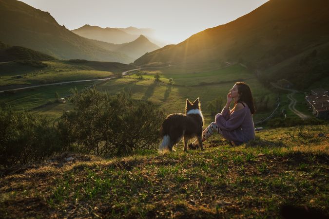 Adult tourist with dog against green forested valley under clear sky in summer
