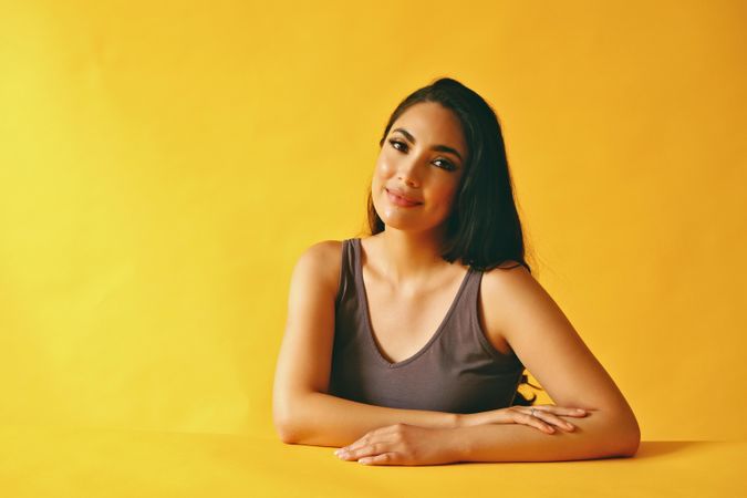Hispanic woman looking wistfully at camera and sitting in yellow room, copy space