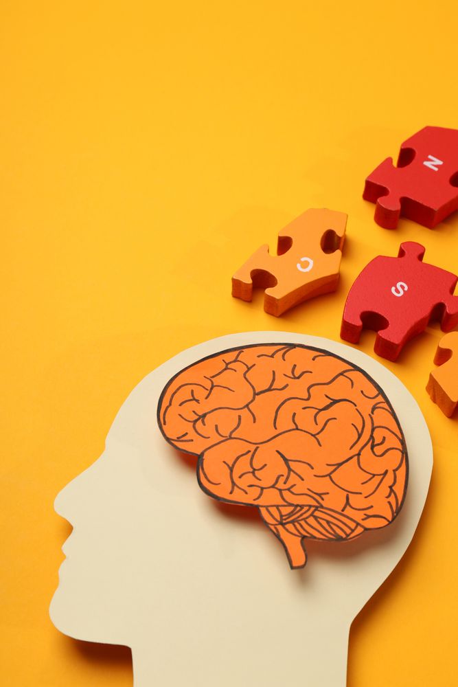 Paper cut out of head with brain & puzzle pieces on orange background, vertical with copy space
