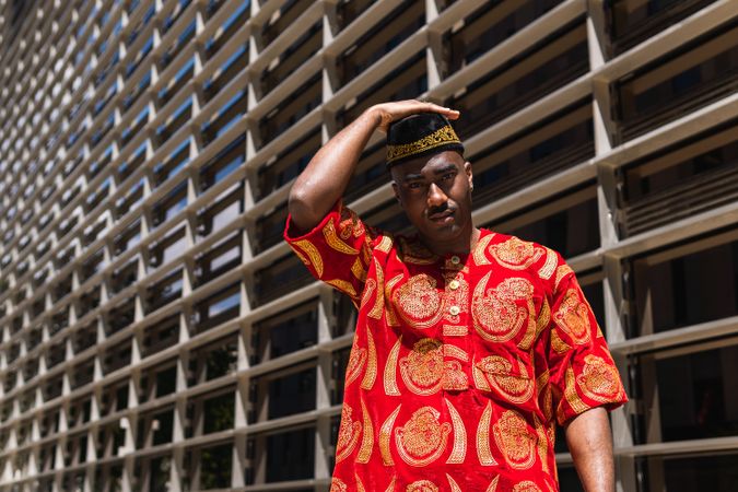 Thoughtful Black man in traditional clothes and headdress near building