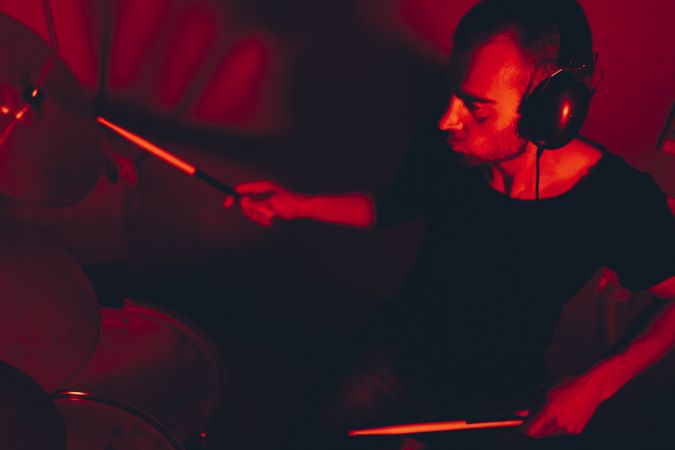 Man with drumsticks playing on drums in redness