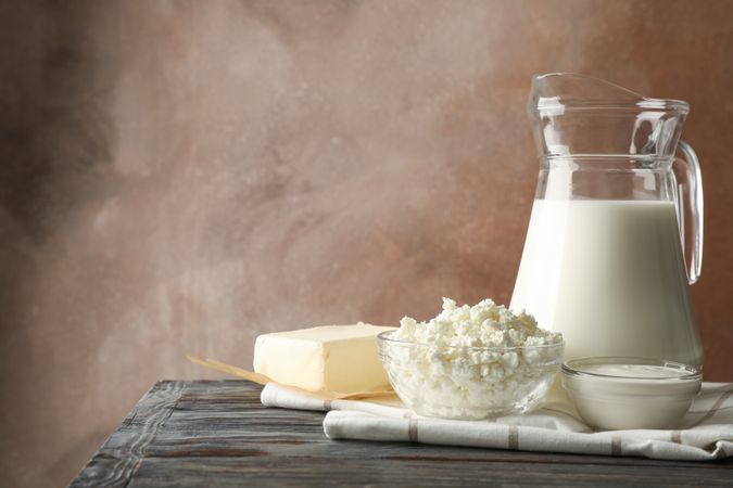 Milk, cottage cheese and butter on wooden table against brown background