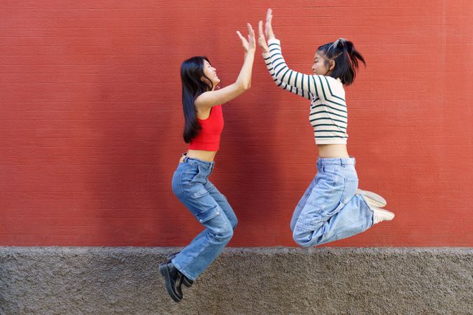 Two women in jeans facing each other jumping and high fiving
