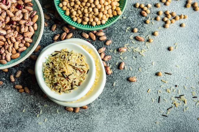 Top view of bowls of dried grains and legumes from pantry on grey counter with copy space
