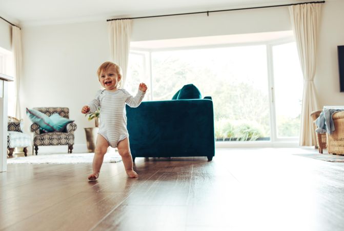 Happy young child learning to walk on wood floor of home